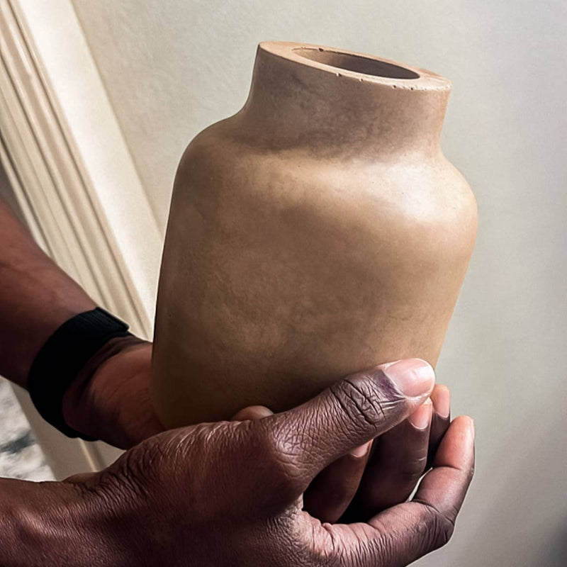 Person holding a brown ceramic vase against a neutral background