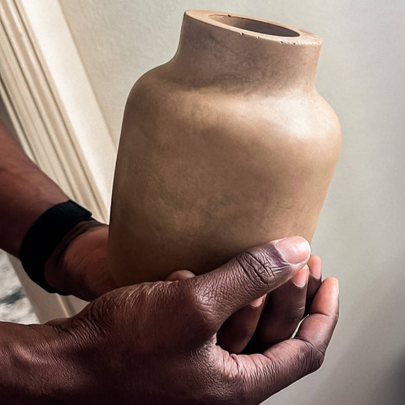 Person holding a brown ceramic vase against a neutral background