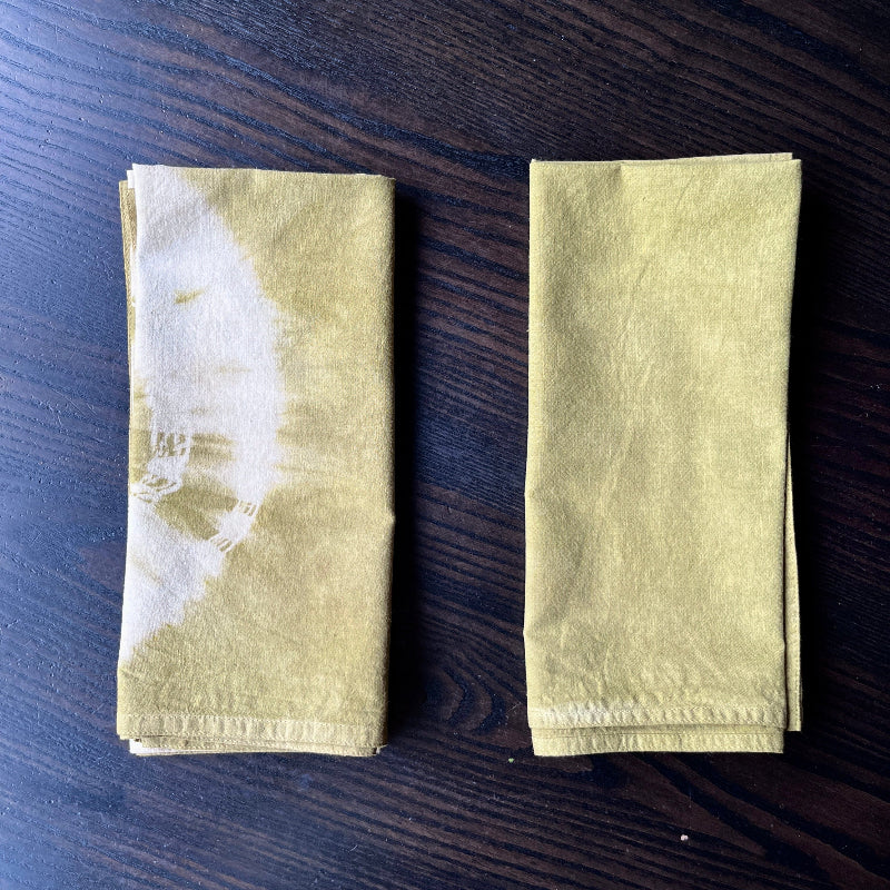 Two folded green napkins on a dark wooden surface