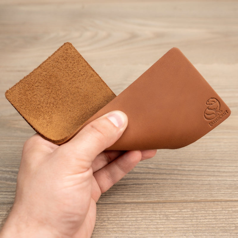 Brown leather honing strop held by a hand on a wooden surface