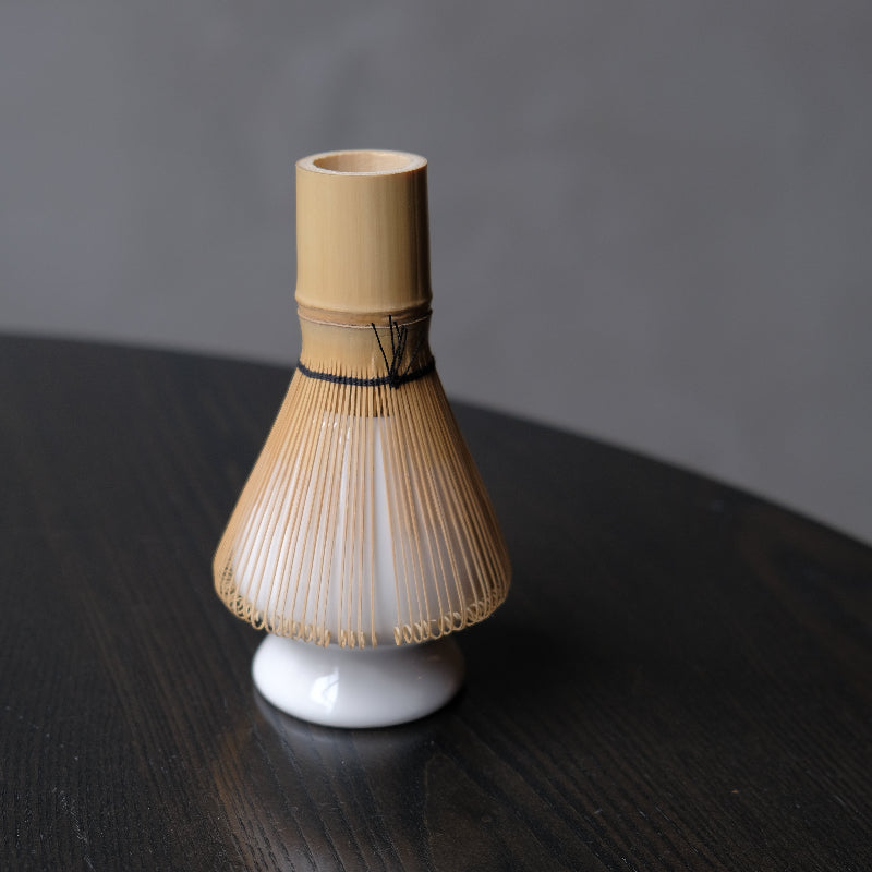 White bamboo whisk holder on a dark wooden surface with a gray background