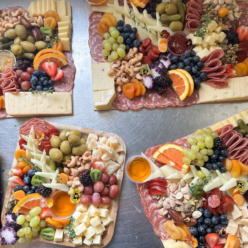 Various charcuterie boards with meats, cheeses, fruits, and nuts on a metal surface.