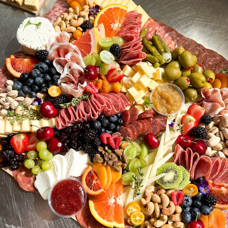 Assorted charcuterie board with meats, cheeses, fruits, and nuts on a metal surface.
