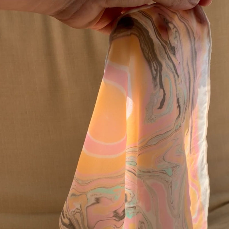 Hand holding a colorful marbled silk against a beige background