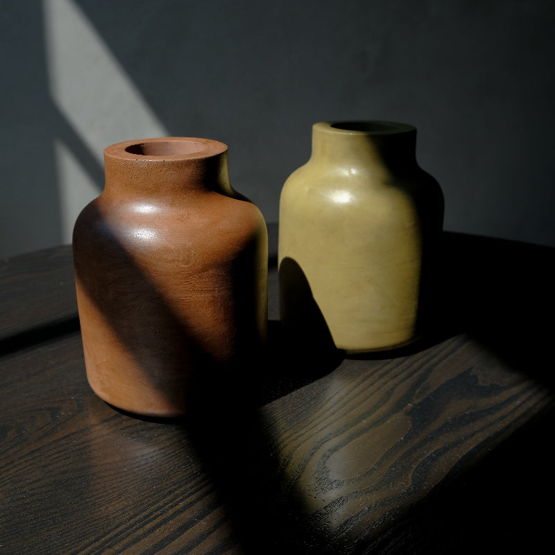 Two concrete vases on a dark surface with a shadow cast by a light source.