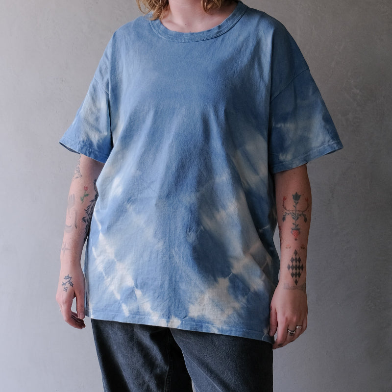 Person wearing a blue tie-dye t-shirt and dark pants against a gray background