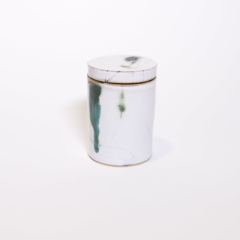 Ceramic storage jar with white glaze on the exterior with highlights of green and turquoise on white background
