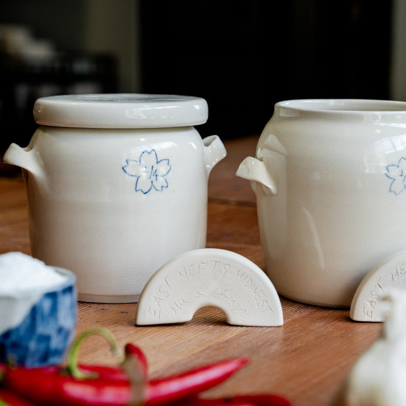 Two ceramic fermenation crocks from Monsoon Pottery with floral inlay designs on a wooden surface.