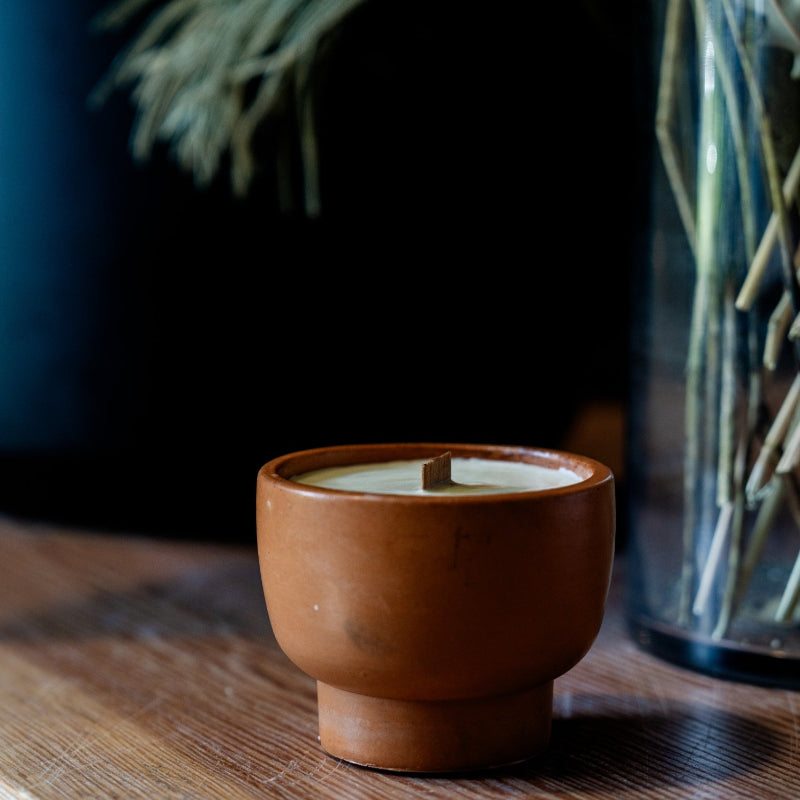 Candle in a terracotta concrete vessel on a wooden surface with a blurred background